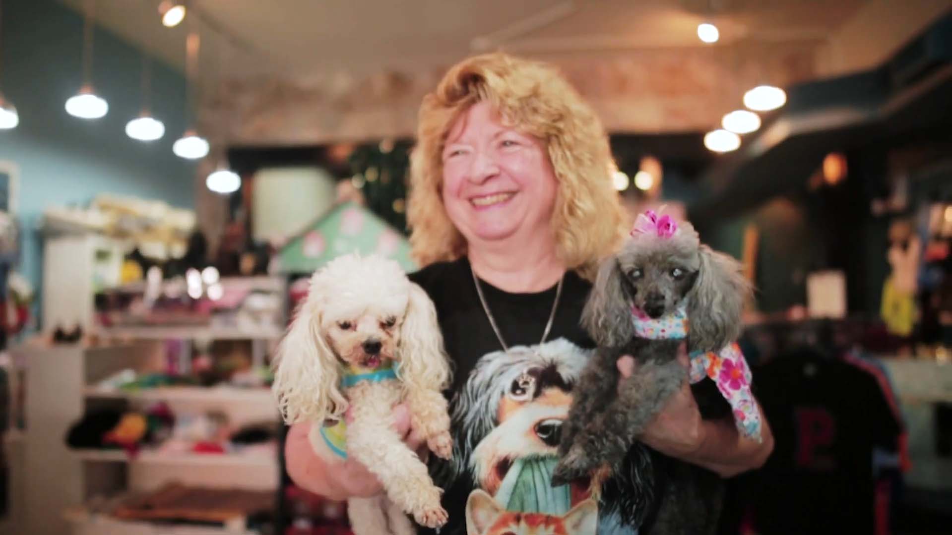 Woman smiling with two dressed-up poodles.
